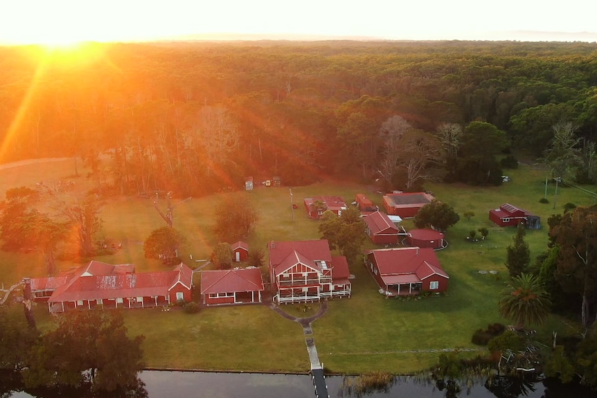 An aerial shot of an hold homestead with red rooves at sunset with a national park in the background