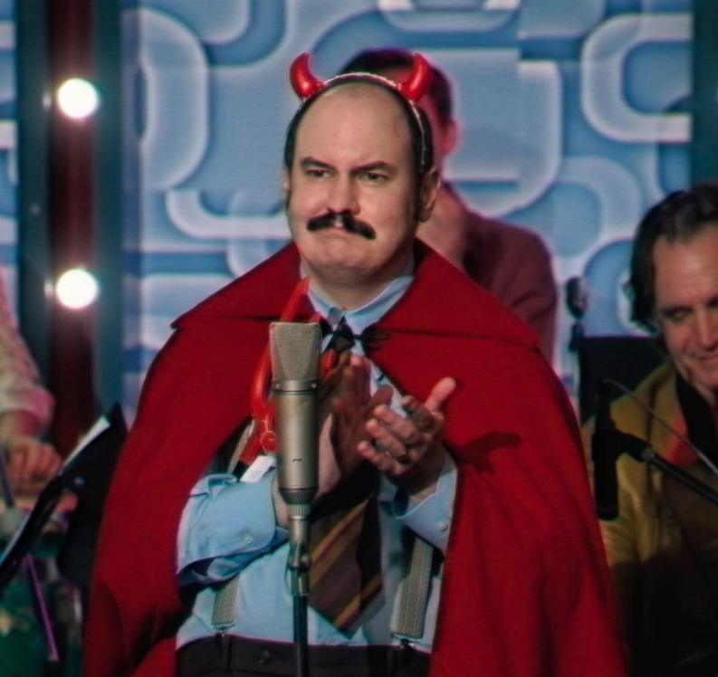 A middle age man with a mustache claps while dressed in a cheap devil costume