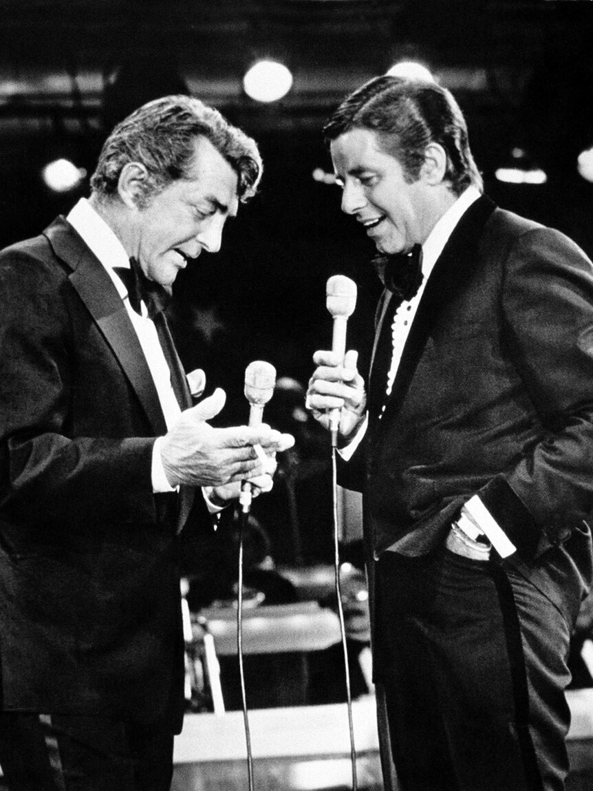 Dean Martin and Jerry Lewis stand next to each other holding microphones.