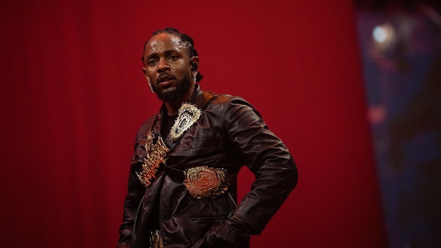 Kendrick Lamar performs live dressed in a military jacket with patches against a red velvet backdrop