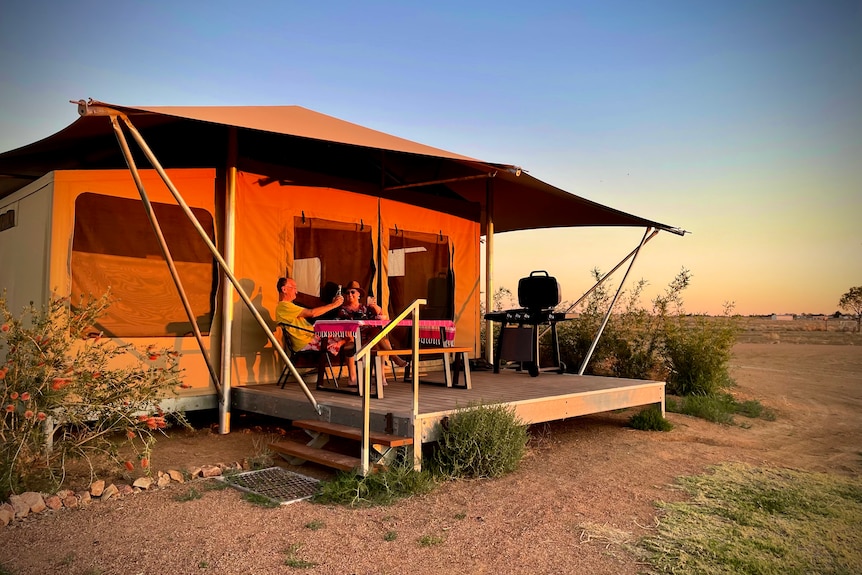 The sunsets on a glamping tent while a couple unwind on their balcony