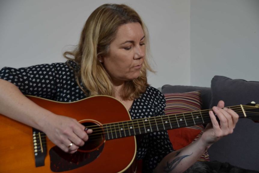 Rebecca Brown playing guitar on her couch.