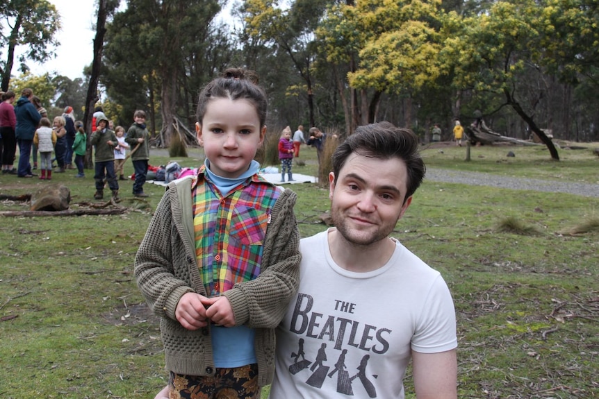 A young father squats next to his son in a bush setting