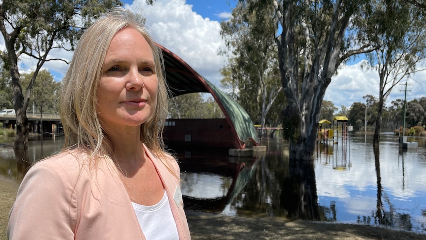 A blonde woman stands in front of a flooded playground.