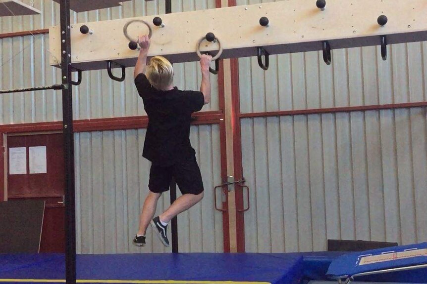 Young man pulling himself across a course hanging from wooden rings