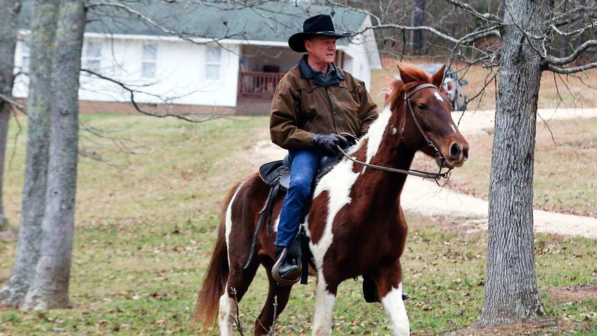 Roy Moore rides his horse among trees.