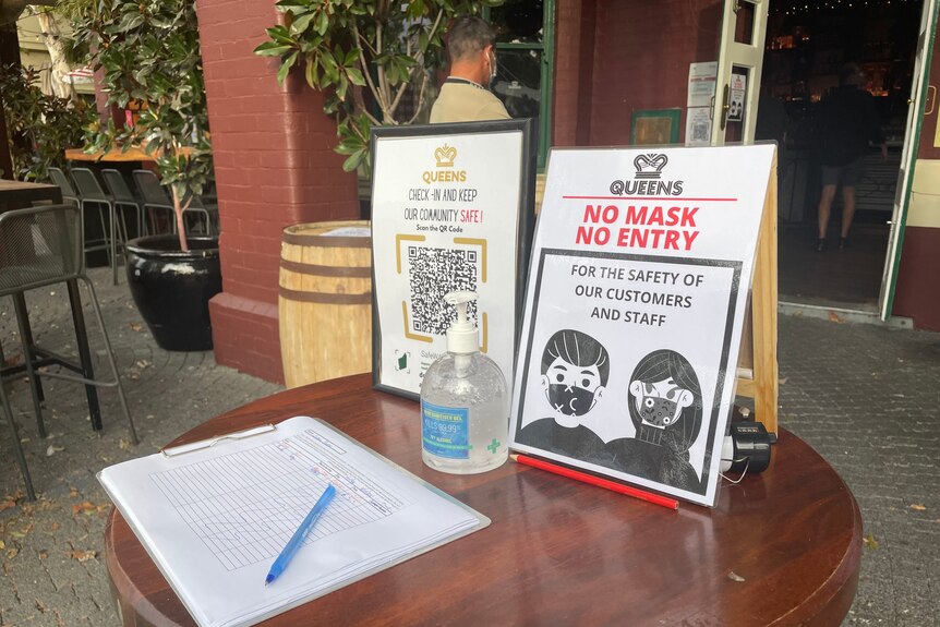 A QR code and sign says 'no mask no entry' on a table out the front of a venue