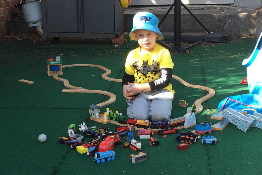 A young boy in a blue hat plays with a toy train set.