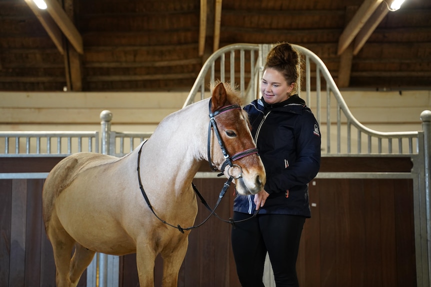 A young woman looks lovingly at a horse inside a stable.