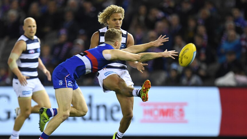 Quinton Narkle attempts to kick for the Cats as a Bulldogs player tries to smother the ball.
