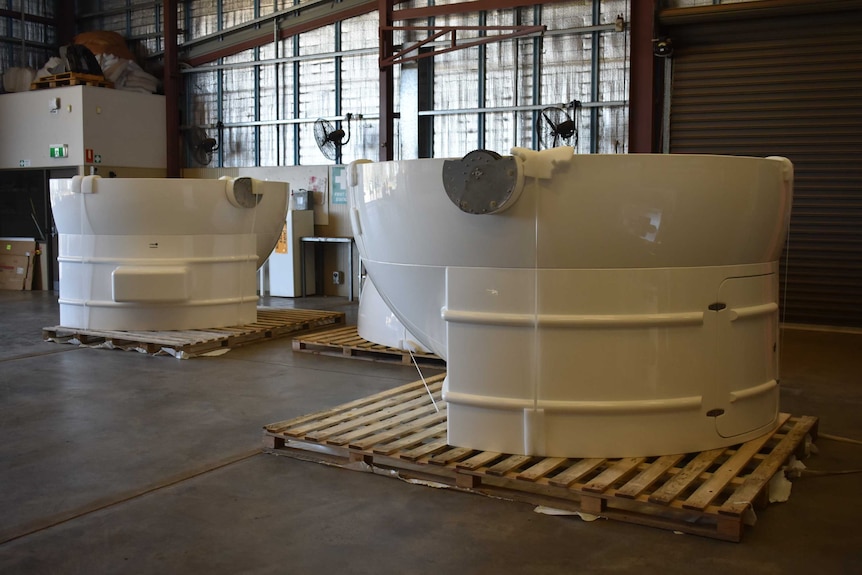 Big white plastic parts of a machine in a shed, they are parts of a clamshell observatory dome.