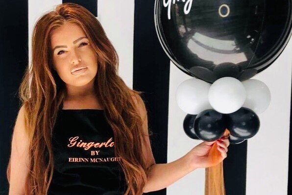 Hairdresser standing beside balloon with salon's name