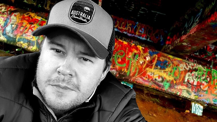 A black and white close-up photo of a man with as colourful background of graffiti.