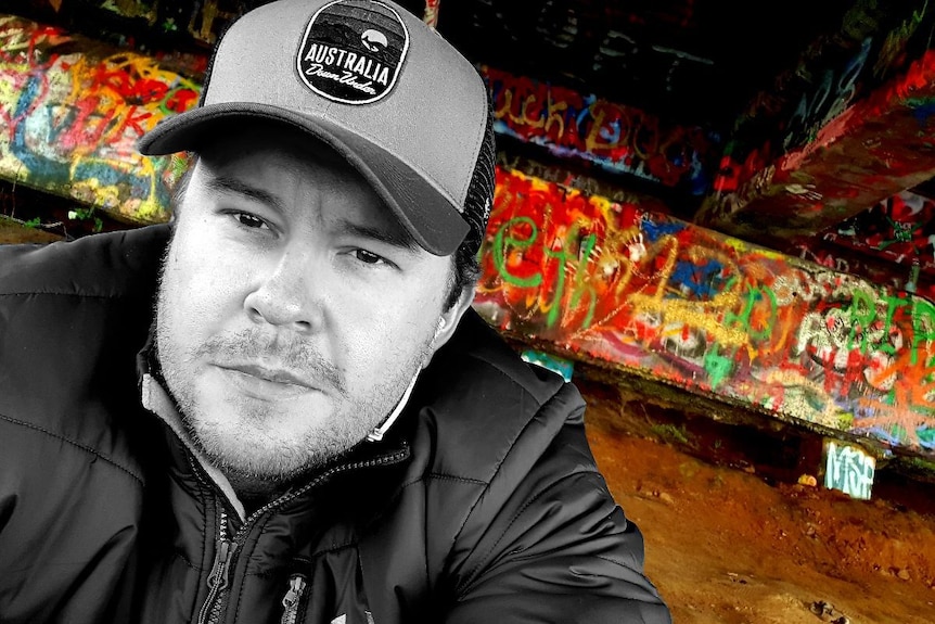 A black and white close-up photo of a man with as colourful background of graffiti.