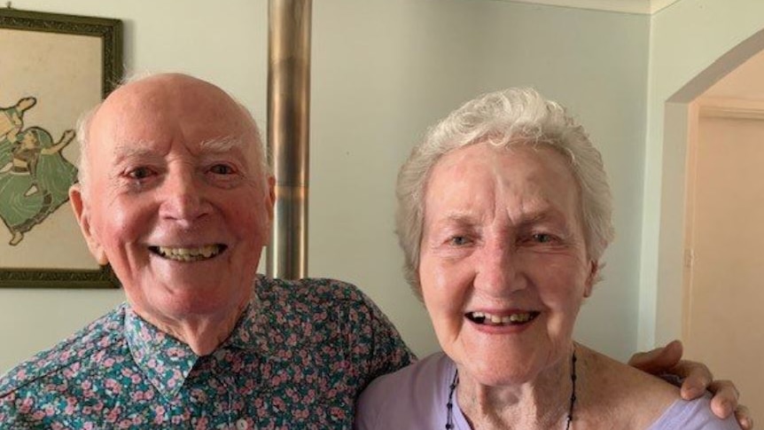 Norm and Joy smile into the camera, his arm around her.