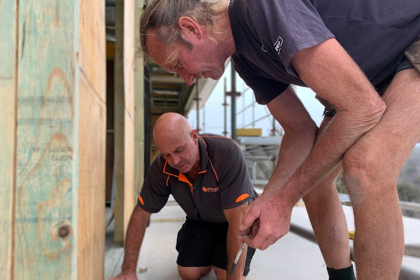 Two men crouched over some tools on scaffolding at a building site