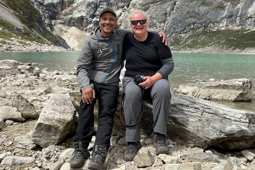 A man and woman sit next to a lake in hiking clothes. 