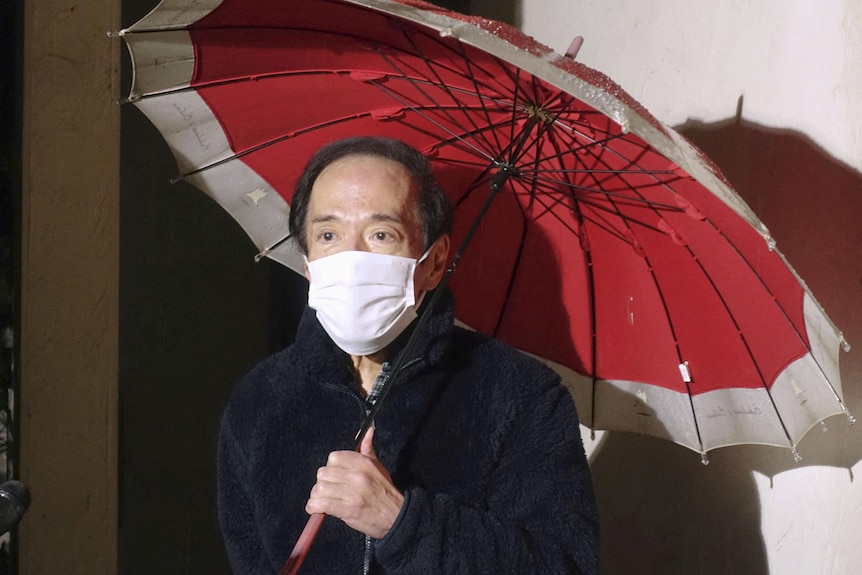Kazuo Ueda holding a red umbrella and wearing a white face mask