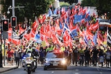 A crowd of union workers carrying red and blue flags march against penalty rate cuts in Brisbane.