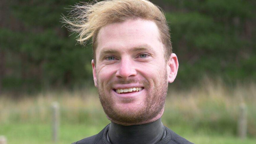 A man wearing a wetsuit looks at the camera