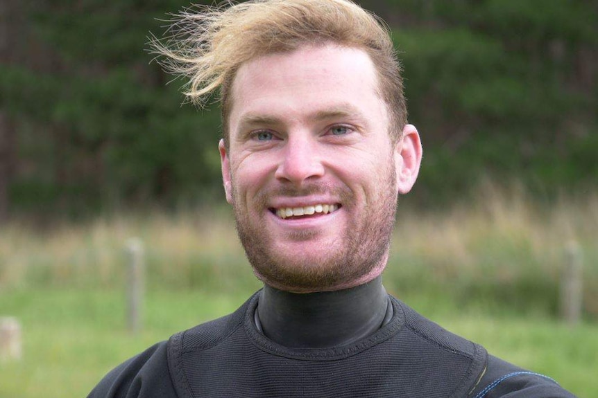 A man wearing a wetsuit looks at the camera