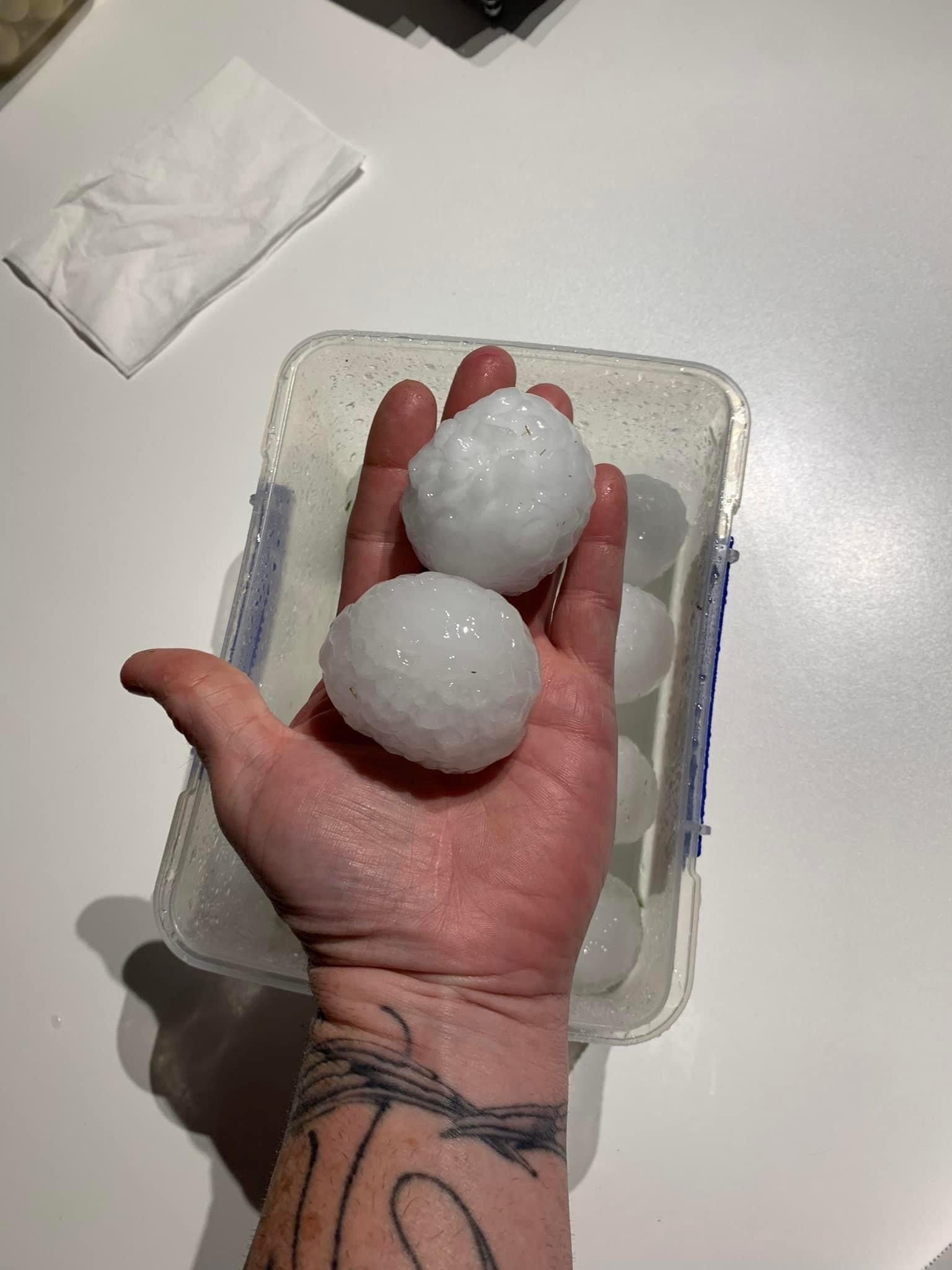Two golf ball sized hail stones sit in a man's hand