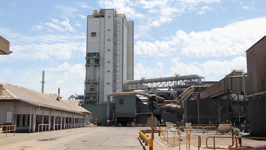 A grey manufacturing plant with an old building to the left and a new, grey tower in the centre