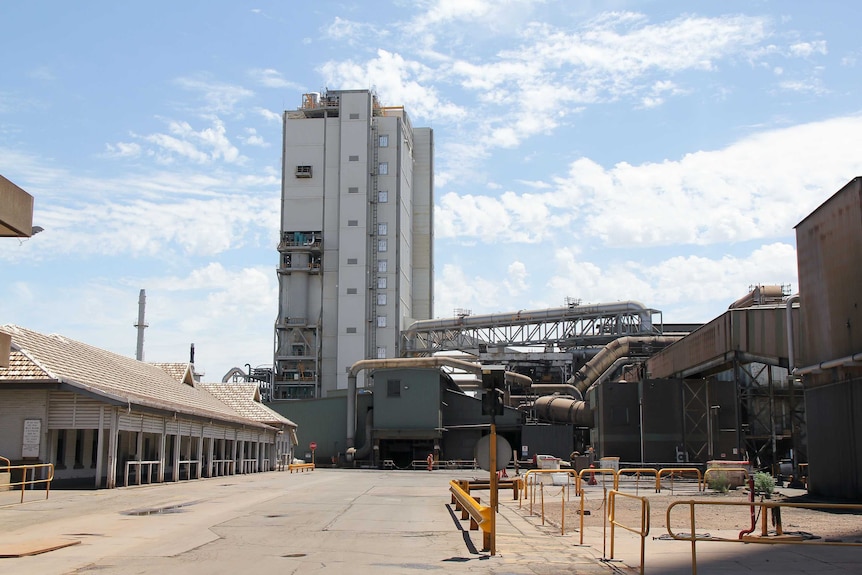 A grey manufacturing plant with an old building to the left and a new, grey tower in the centre