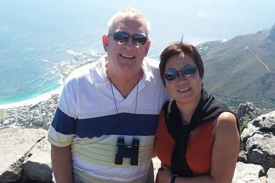 A man and woman smiling with a beach in the background.