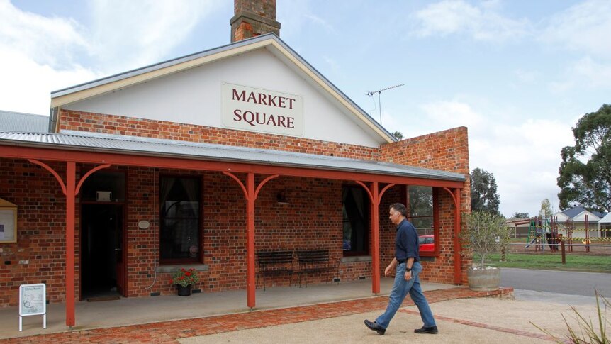 A man in jeans an a navy blue collared shirt walks into a red brick building.