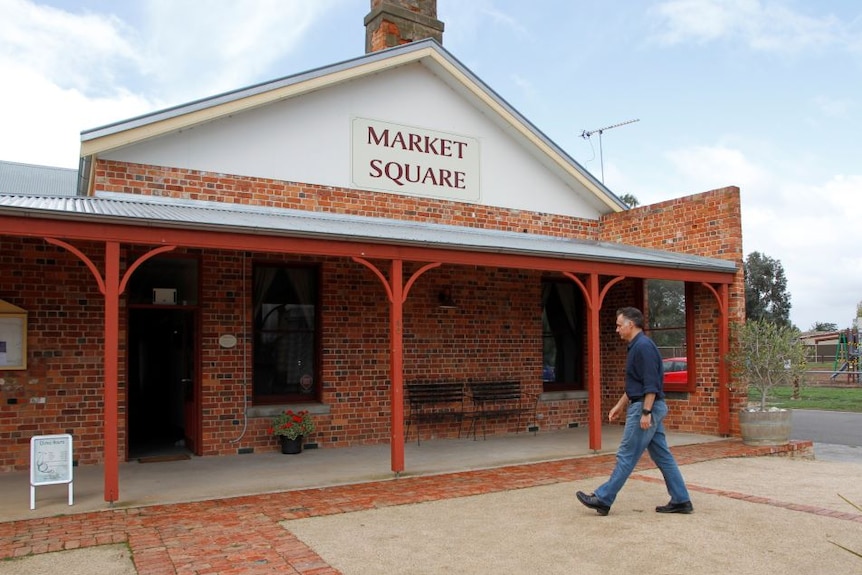 A man in jeans an a navy blue collared shirt walks into a red brick building.