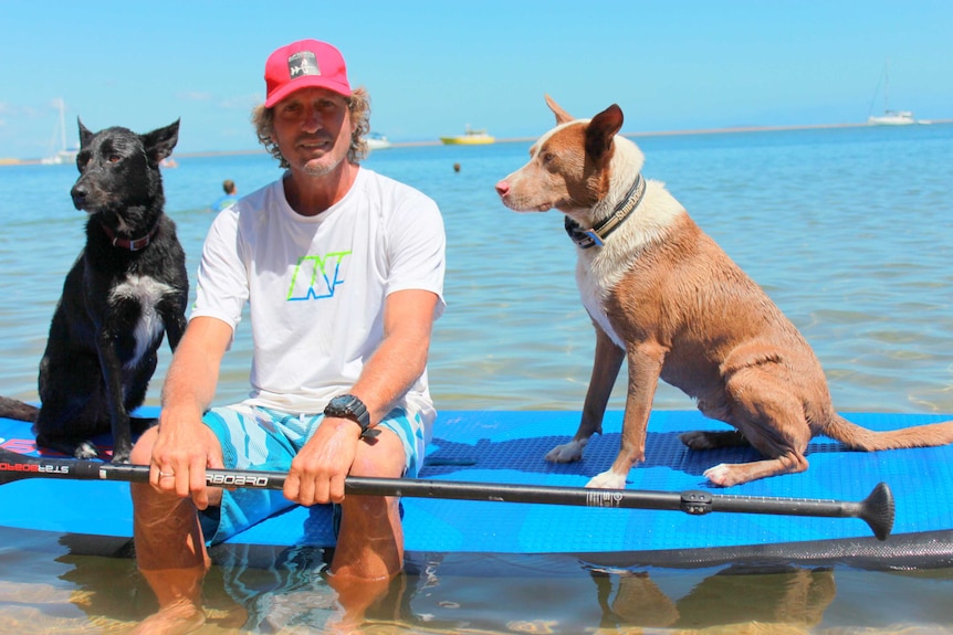 Chris De Aboitiz sitting on a paddle board with his two dogs