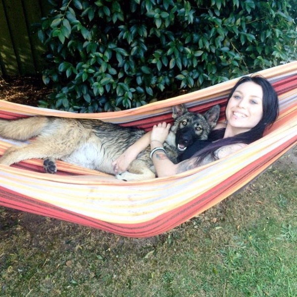 A young woman relaxes in a hammock while hugging a large smiling dog.
