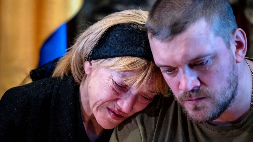 A woman cries as she leans on the soldier of a younger man during a funeral in Ukraine.