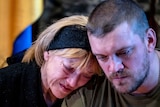 A woman cries as she leans on the soldier of a younger man during a funeral in Ukraine.