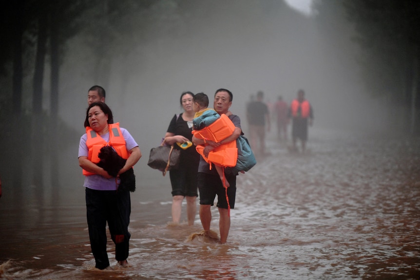 People in lifejackets walk through ankle-deep floodwater.