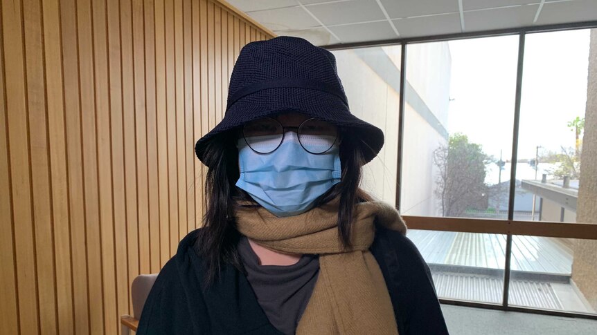 A woman in a mask, hat and glasses disguises her face.