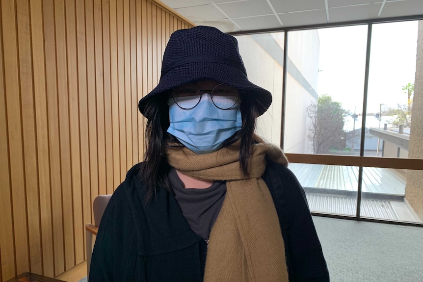 A woman in a mask, hat and glasses disguises her face.