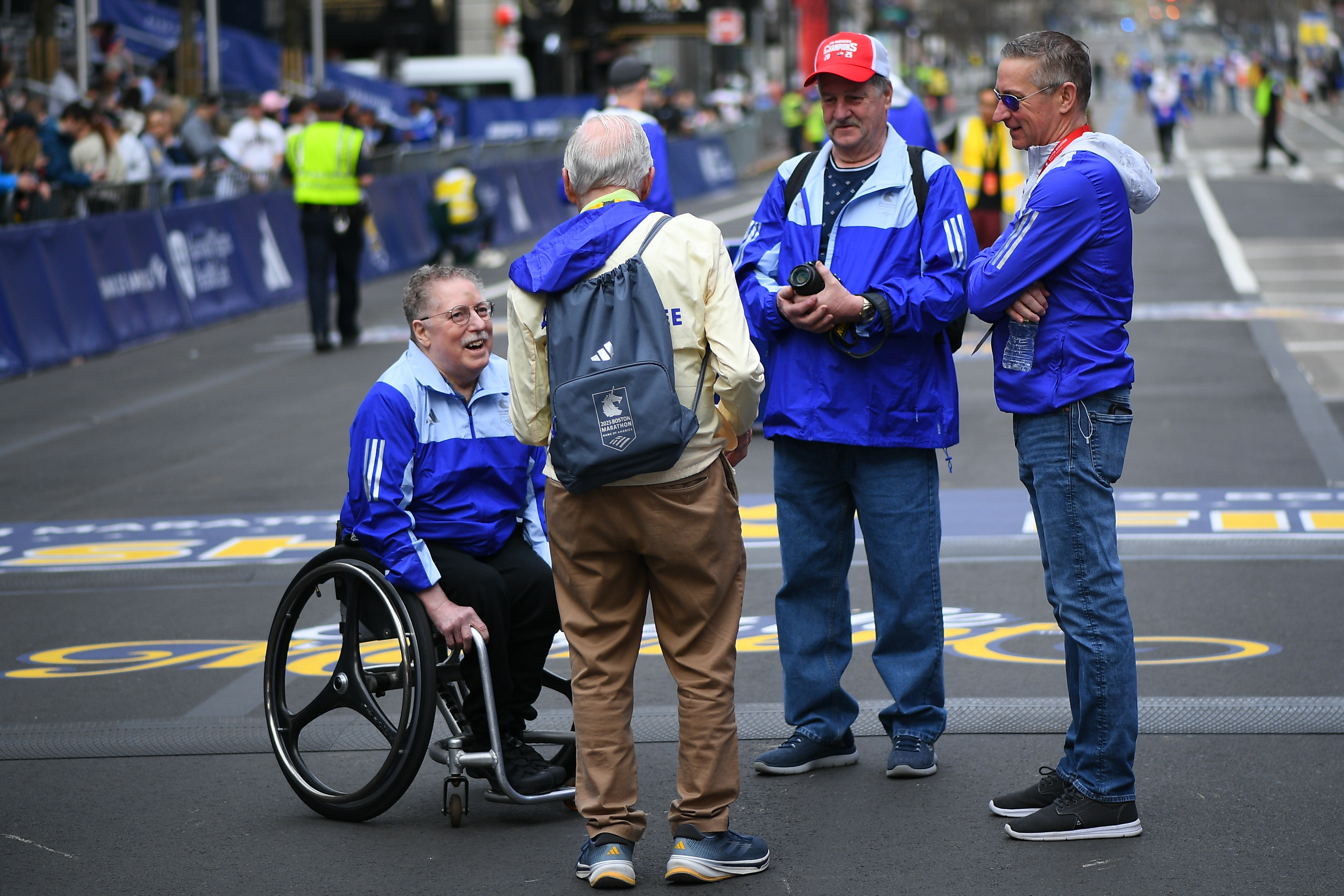 Um homem idoso em cadeira de rodas fala com um grupo de oficiais da maratona.