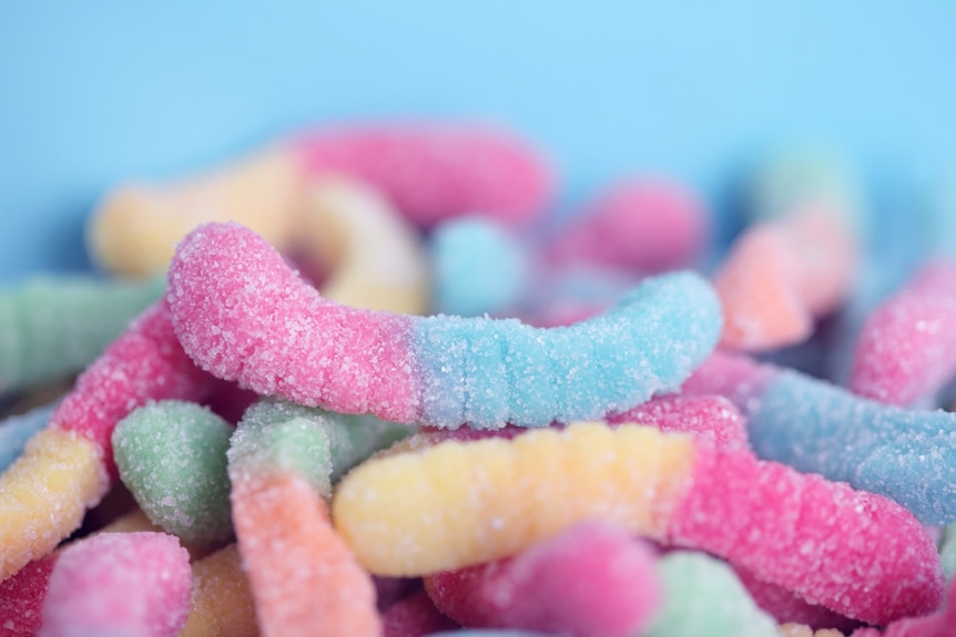 Close-up of pink and green, sugar-coated worm-like sour lollies