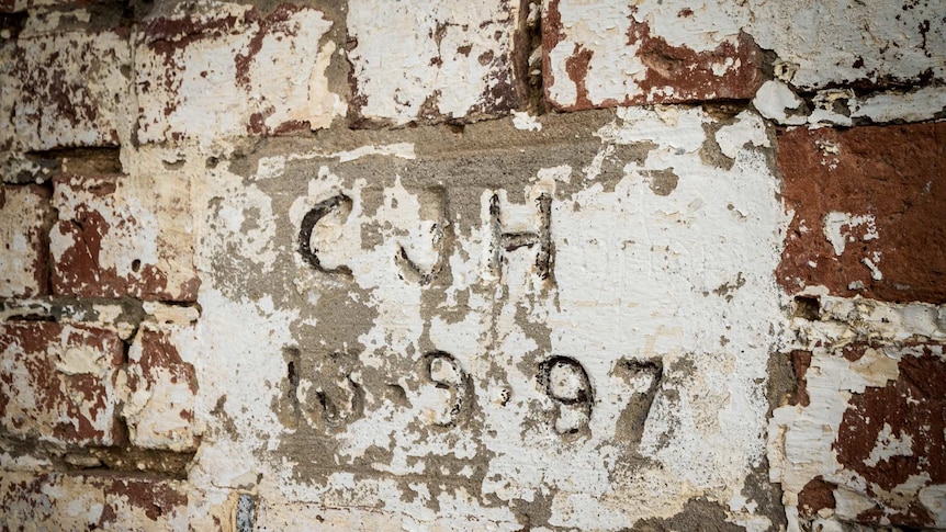 A stone set into a brick wall, partially covered in flaking white paint, with CJH 13.9.97 carved into it