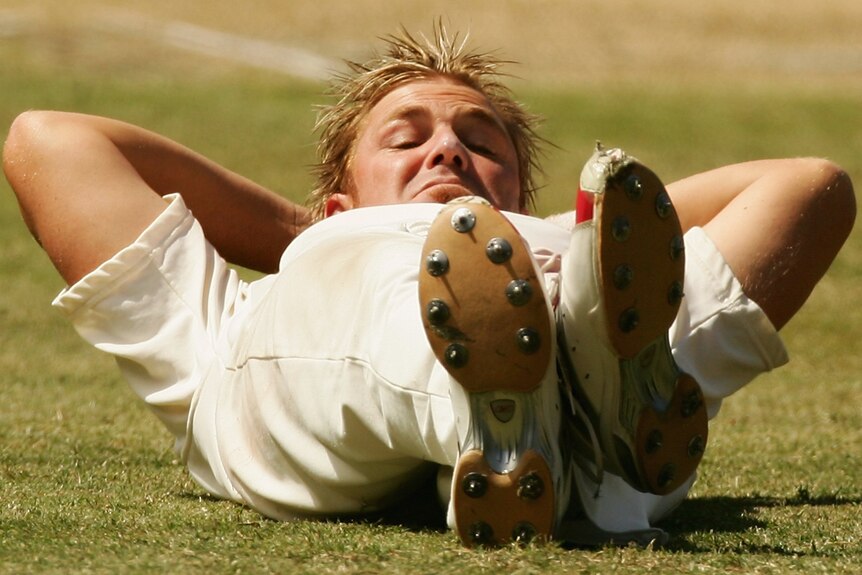 Shane Warne lies on the pitch in mock relaxation while waiting on a match delay