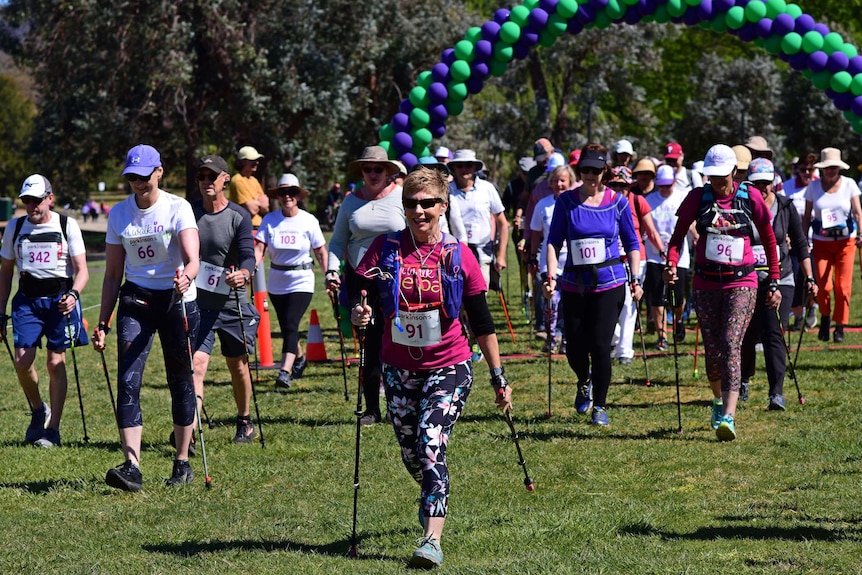 People in athletic clothing holding walking poles and wearing racing bibs walk together.