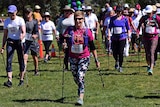 People in athletic clothing holding walking poles and wearing racing bibs walk together.