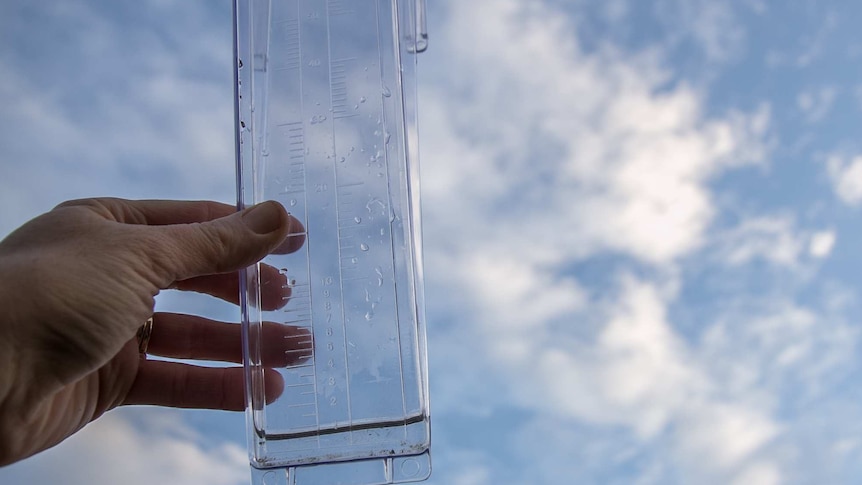 Close up of a hand holding a rain gauge up against the sky holding 1mm of rain