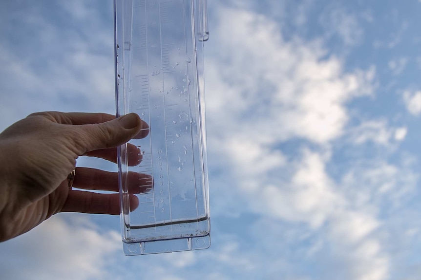 Close up of a hand holding a rain gauge up against the sky holding 1mm of rain