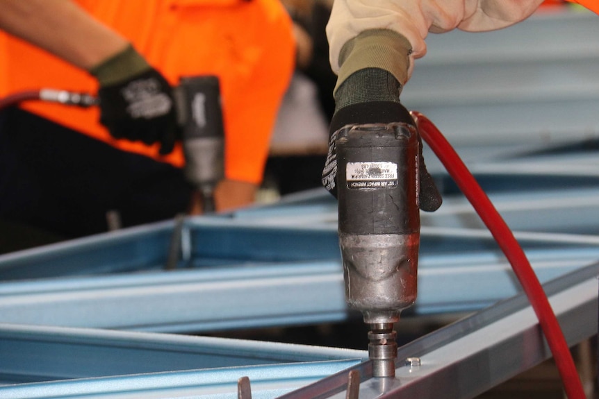 A man holding a drill works on a steel frame inside a prison centre