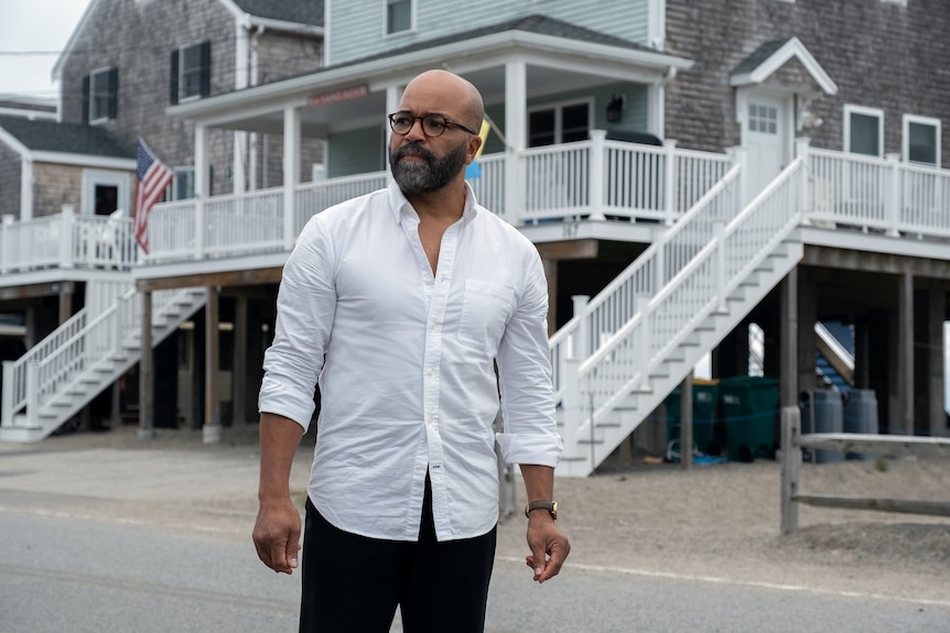 Jeffrey Wright as Monk wearing a white buttoned shirt, standing in front of a property with an American flag in the distance