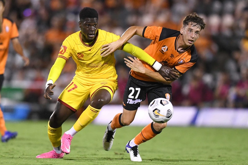 Mohamed Toure, left in a yellow shirt, holds a hand across Kai Trewin in an orange kit