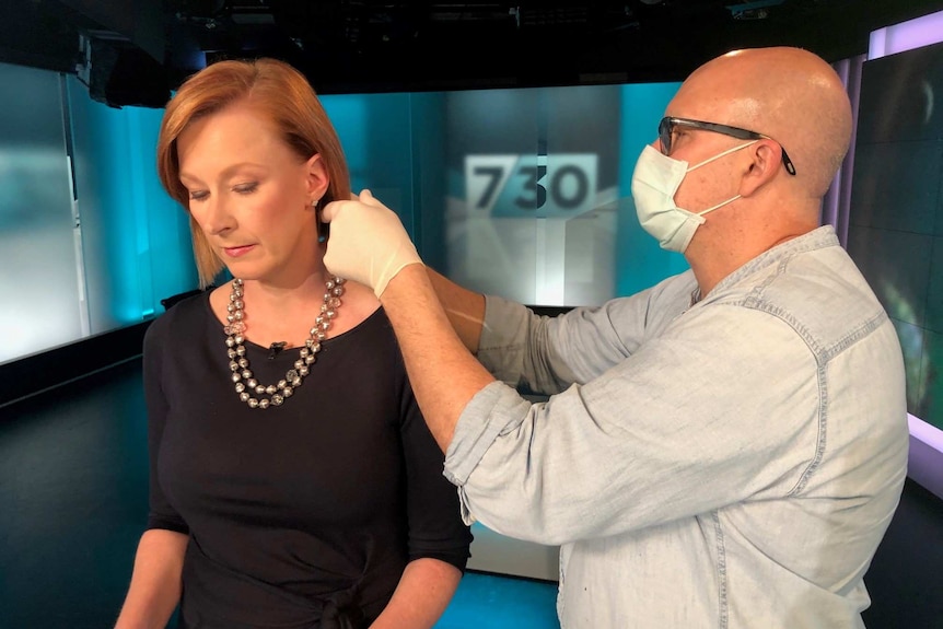 Make-up artist wearing mask and rubber gloves combing Sales hair in studio.